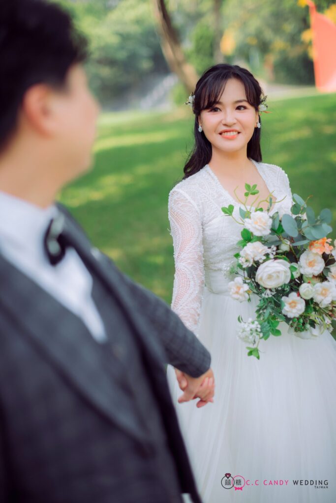 綠地上手捧白色花束的新娘望向新郎｜新竹婚紗工作室
