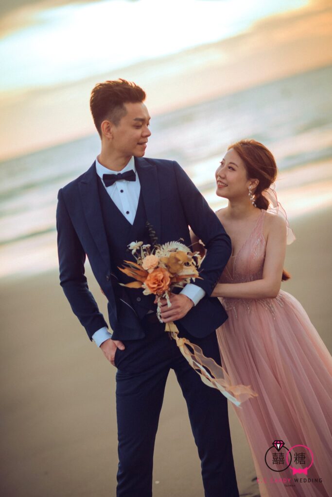 婚紗攝影推薦・夕陽海邊新郎手持花束擁著粉紗新娘 夕陽海邊新郎手持花束擁著粉紗新娘|婚紗照姿勢