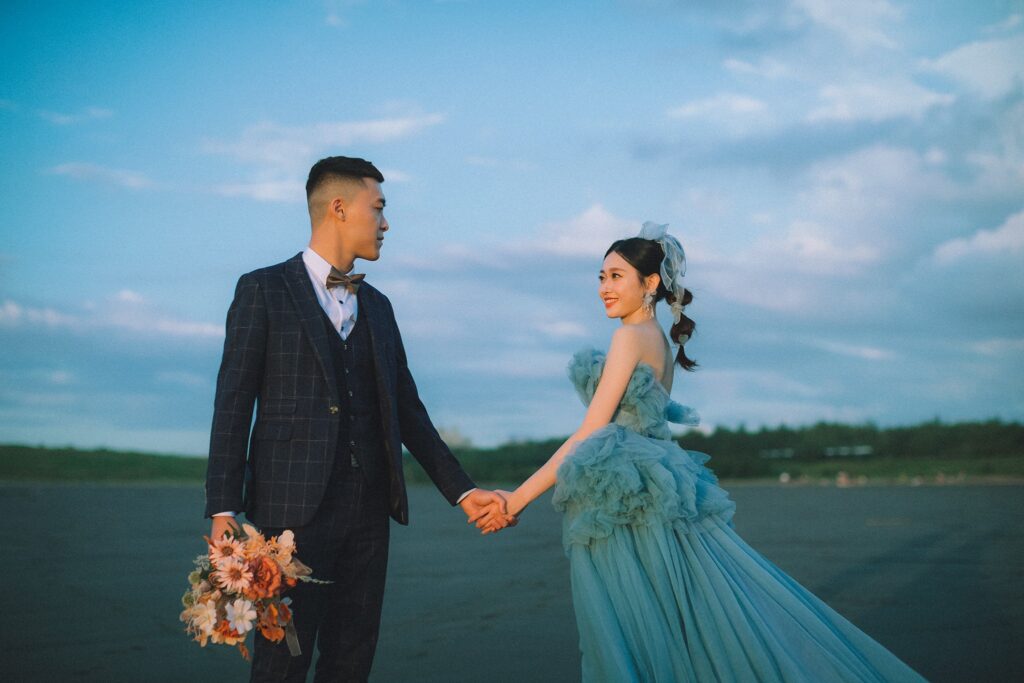 海邊草原上牽手的新人，新娘穿藍色禮服｜婚紗照姿勢