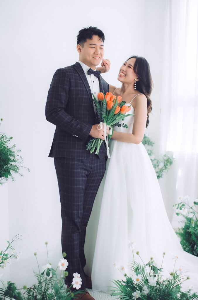 白色花藝棚景婚紗照，新人手捧橘色花束｜新竹婚紗包套價格