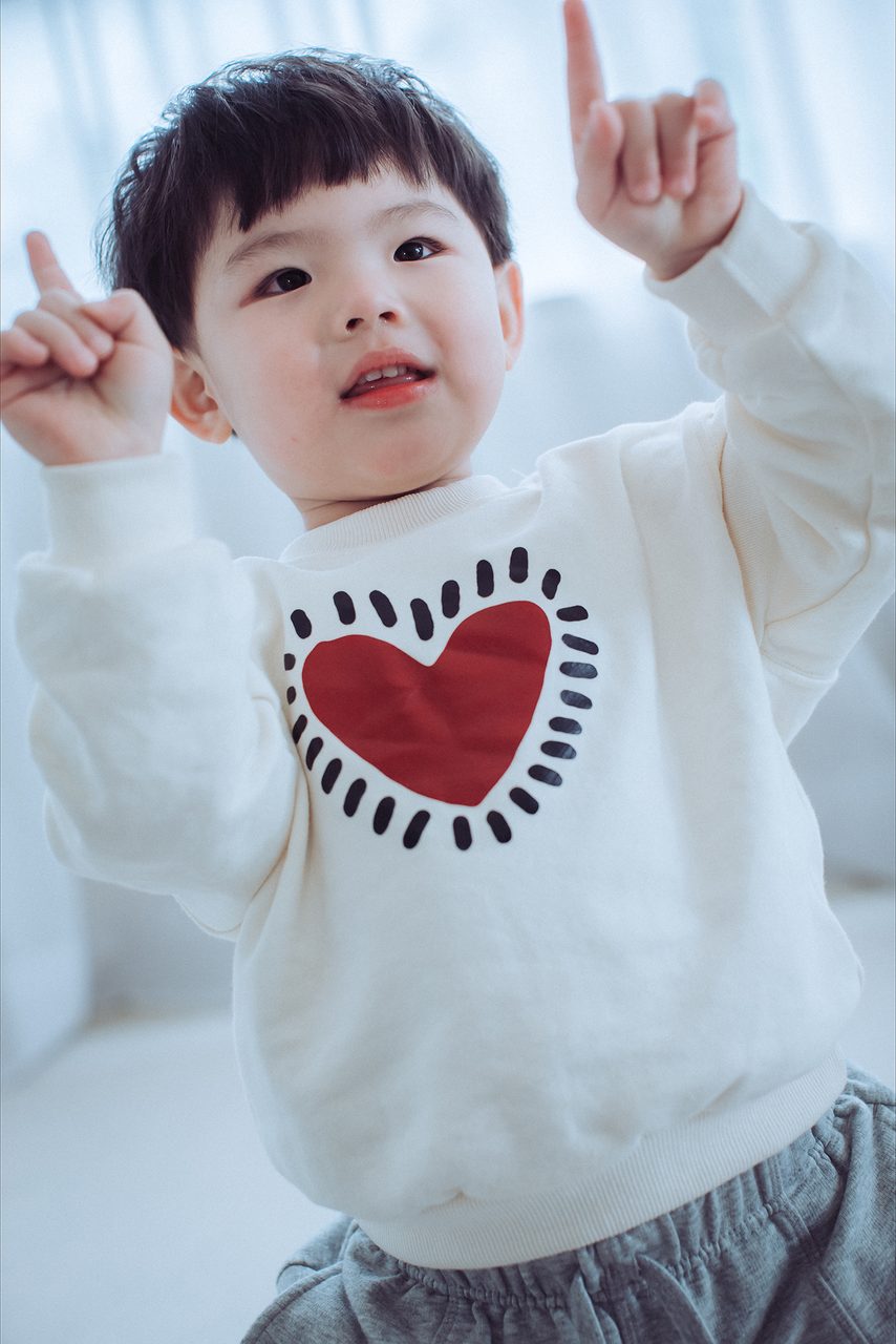 孩子動個不停,快門先拉快一點 小男孩舉起雙手比出手勢,穿著愛心毛衣,笑得很開心