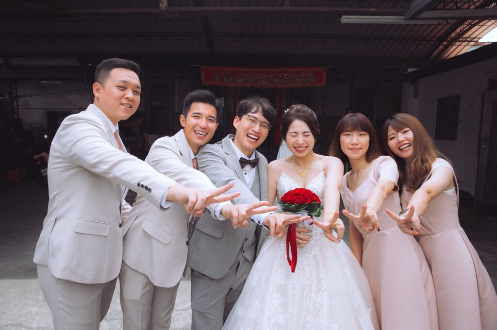 結婚當天穿蓬裙蕾絲白紗的新娘手捧紅玫瑰，與伴郎伴娘開心合照