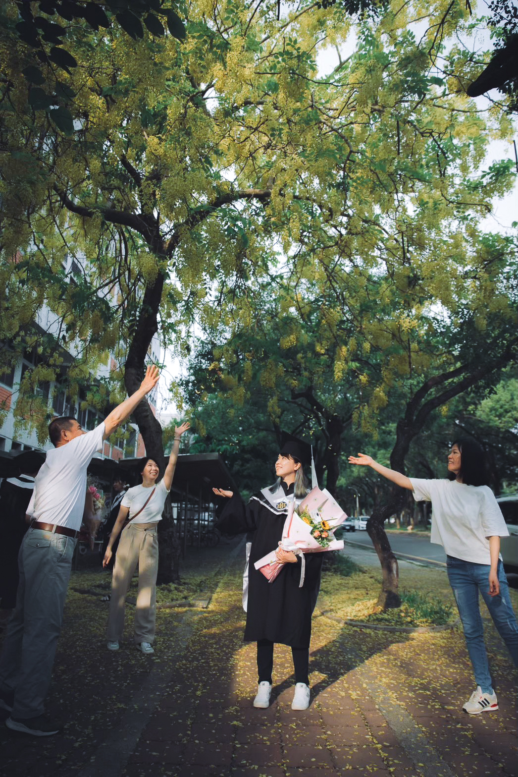 畢業照家人互動:一起拋花瓣 畢業照家人合照互動:全家伸手拋起阿勃勒花瓣,畢業生站中間