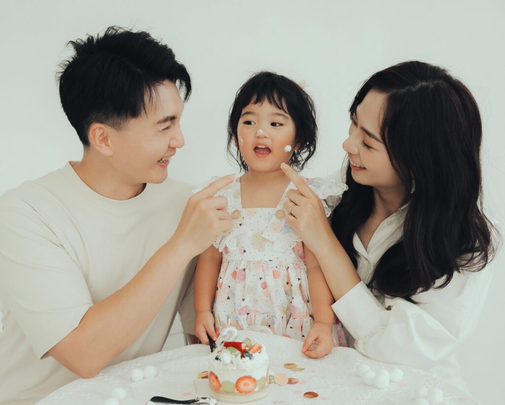生日全家福|臉上點奶油 爸媽在兩歲女兒臉上點奶油,桌上放著草莓生日蛋糕