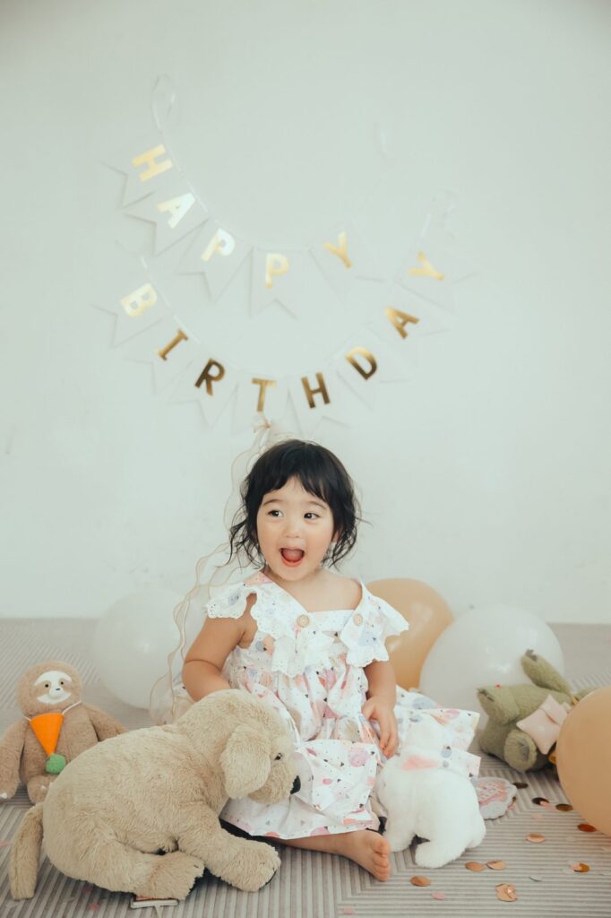 兩歲生日寫真|玩偶與氣球 兩歲女孩坐在地墊上靠著大狗玩偶,旁邊有氣球和金色亮片