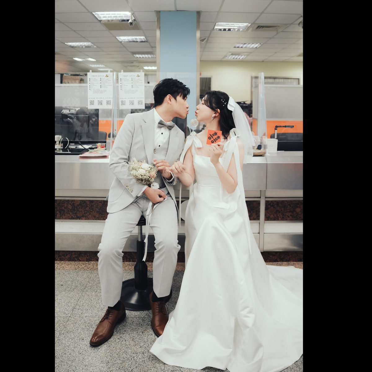 結婚登記拍照姿勢|櫃台前嘟嘴親親 結婚登記拍照姿勢,新人坐在戶政櫃台前嘟嘴親親,新娘拿著囍字