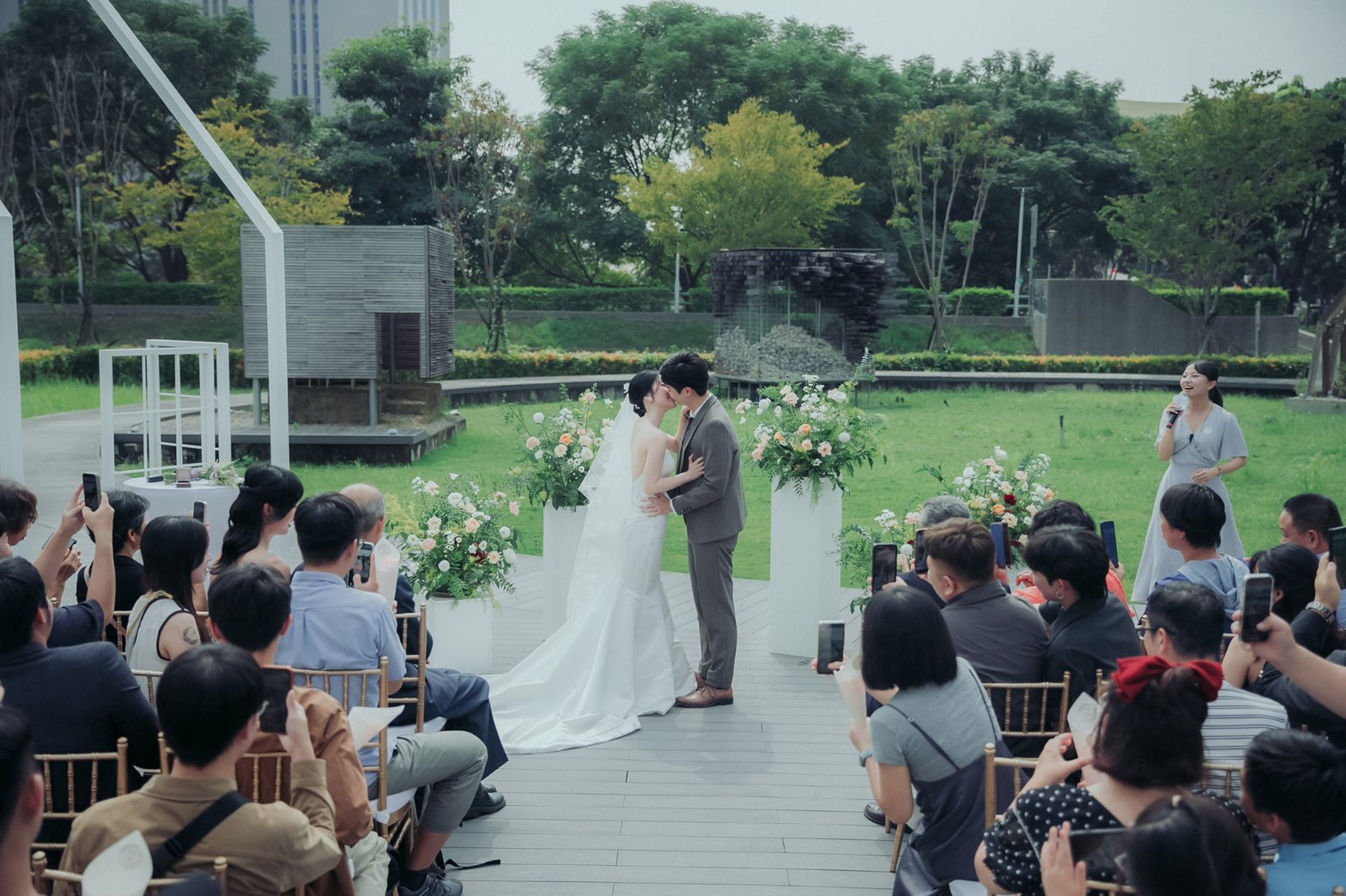 戶外證婚親吻：新人在花柱前擁吻，賓客舉起手機拍照