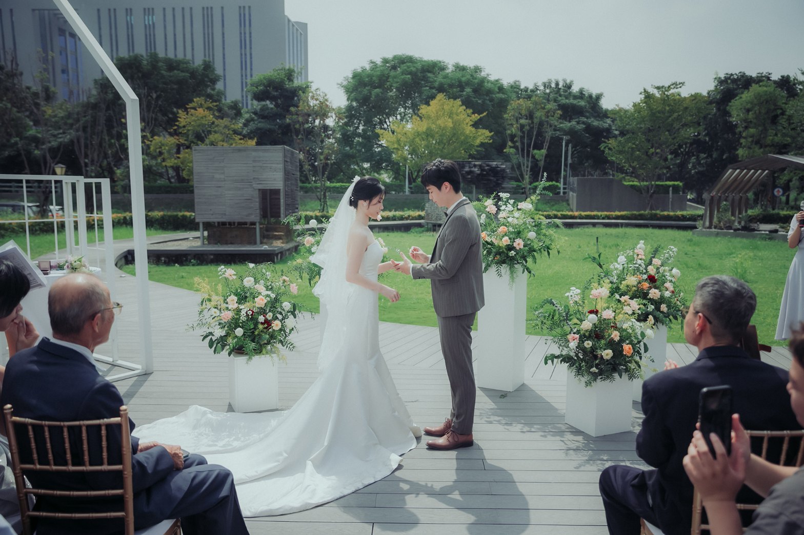 白紗長裙襬戶外實拍 白紗長裙襬拖在平台上,新郎為新娘戴上戒指,禮服版型在戶外的樣子