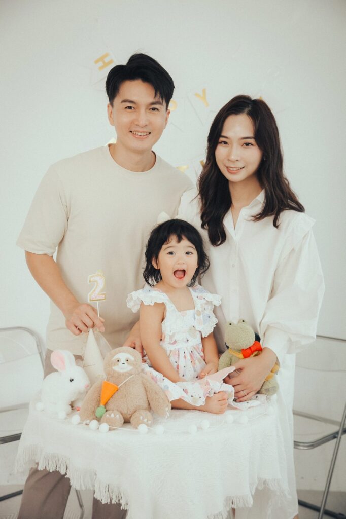 兩歲生日全家福|室內佈置 爸媽陪兩歲女兒在生日佈置前的全家福,桌上擺著玩偶和數字 2
